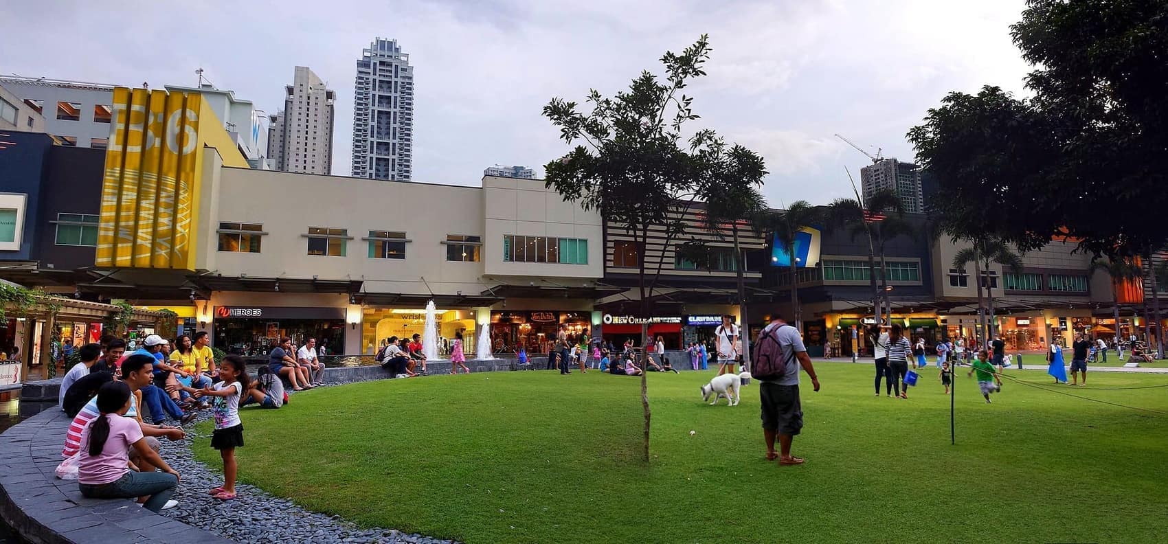 Bonifacio High Street at dusk: the central lawn, a dog off the leash, families spilling out of the shopfronts