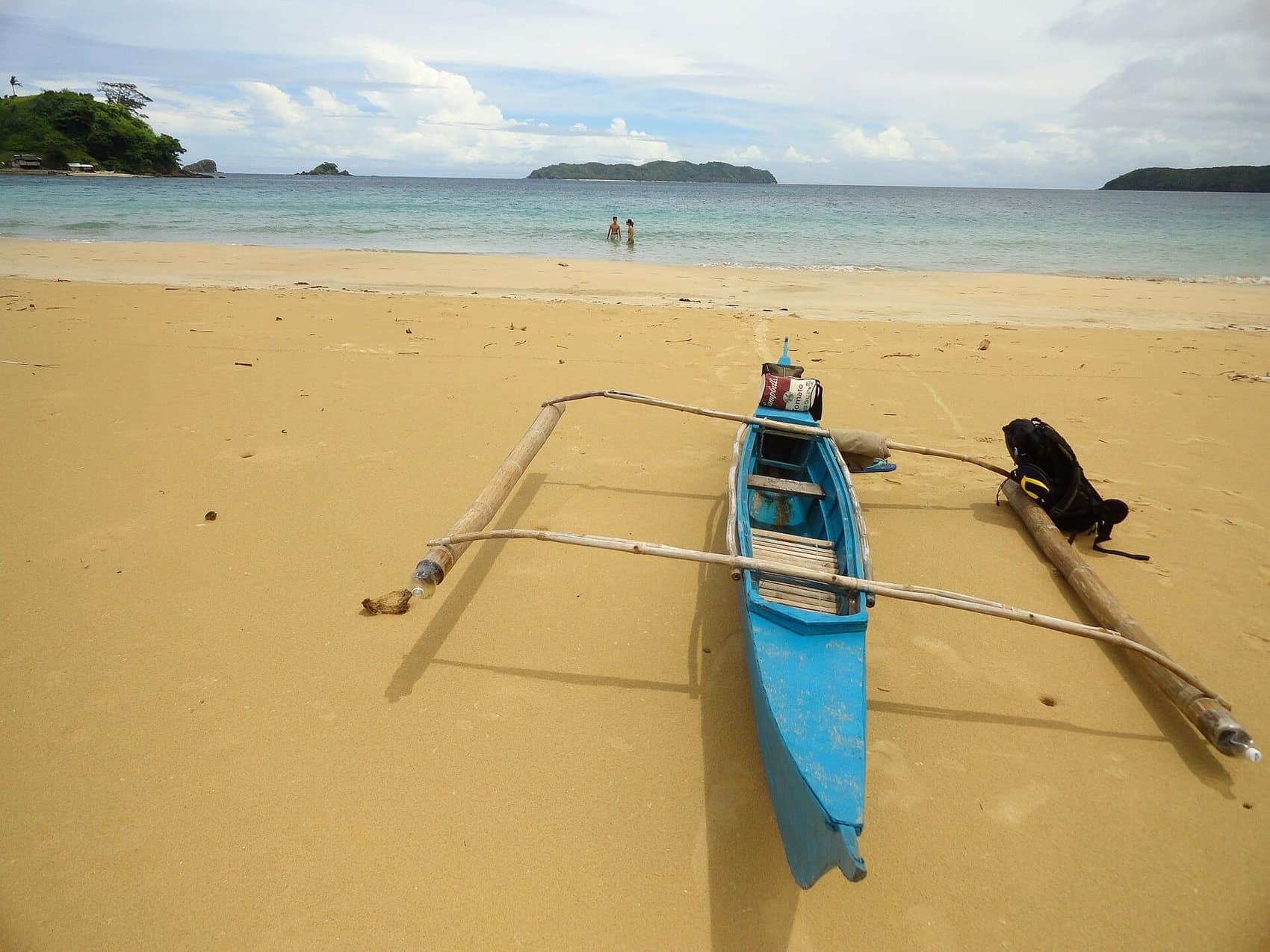 A bangka pulled up on Nacpan's sand, headland in the distance
