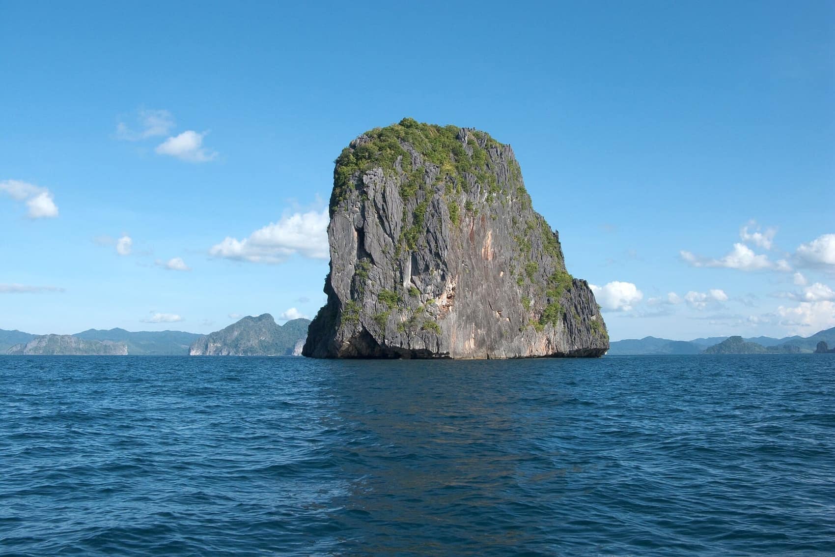 A lone limestone monolith standing in open water, the silhouette that defines Bacuit Bay