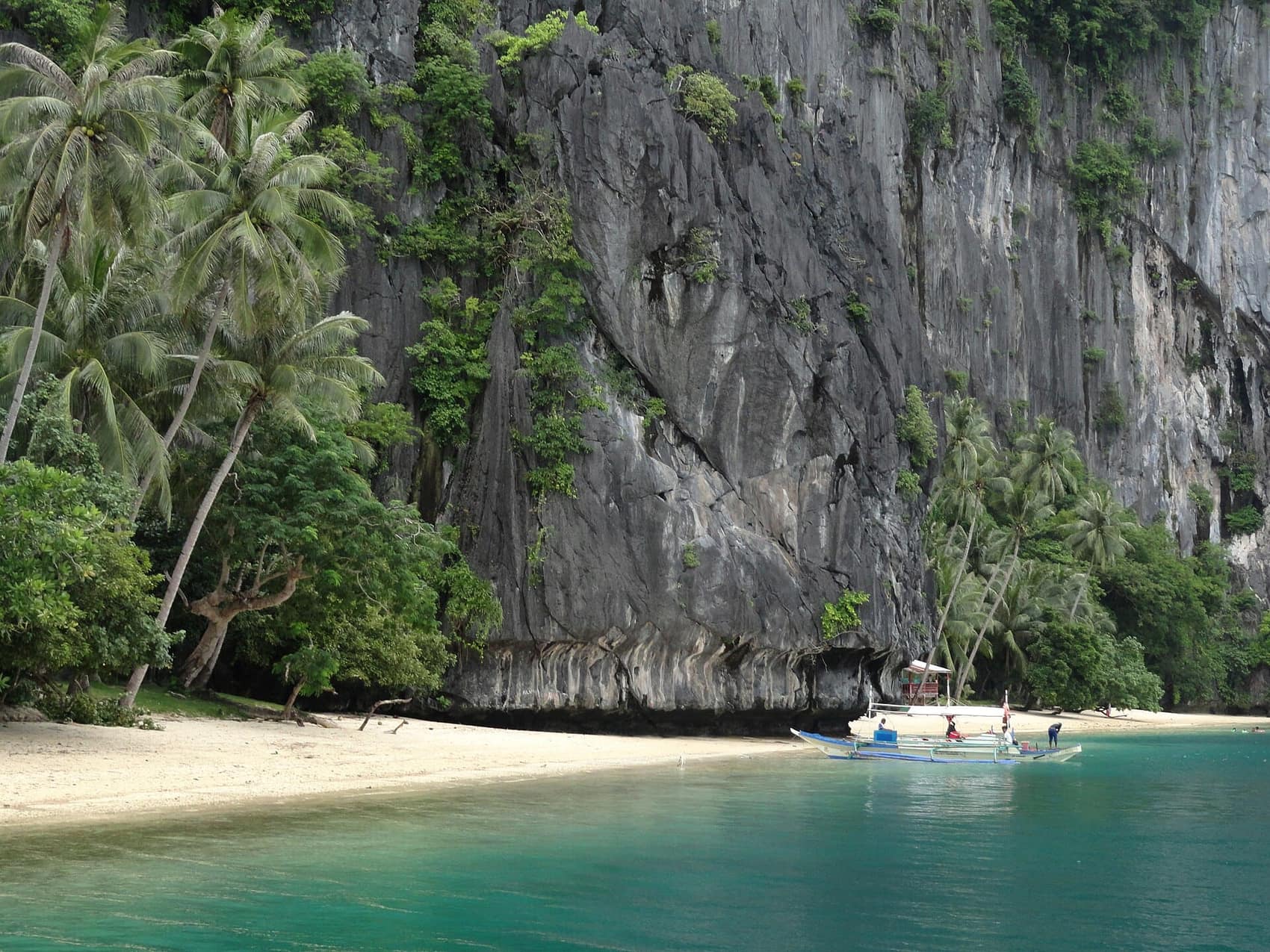 Pinagbuyutan Island: boats pulled up on the beach at the foot of a towering cliff