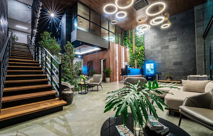 Double-height lobby: dark stone, ring lights, stairs threaded with greenery