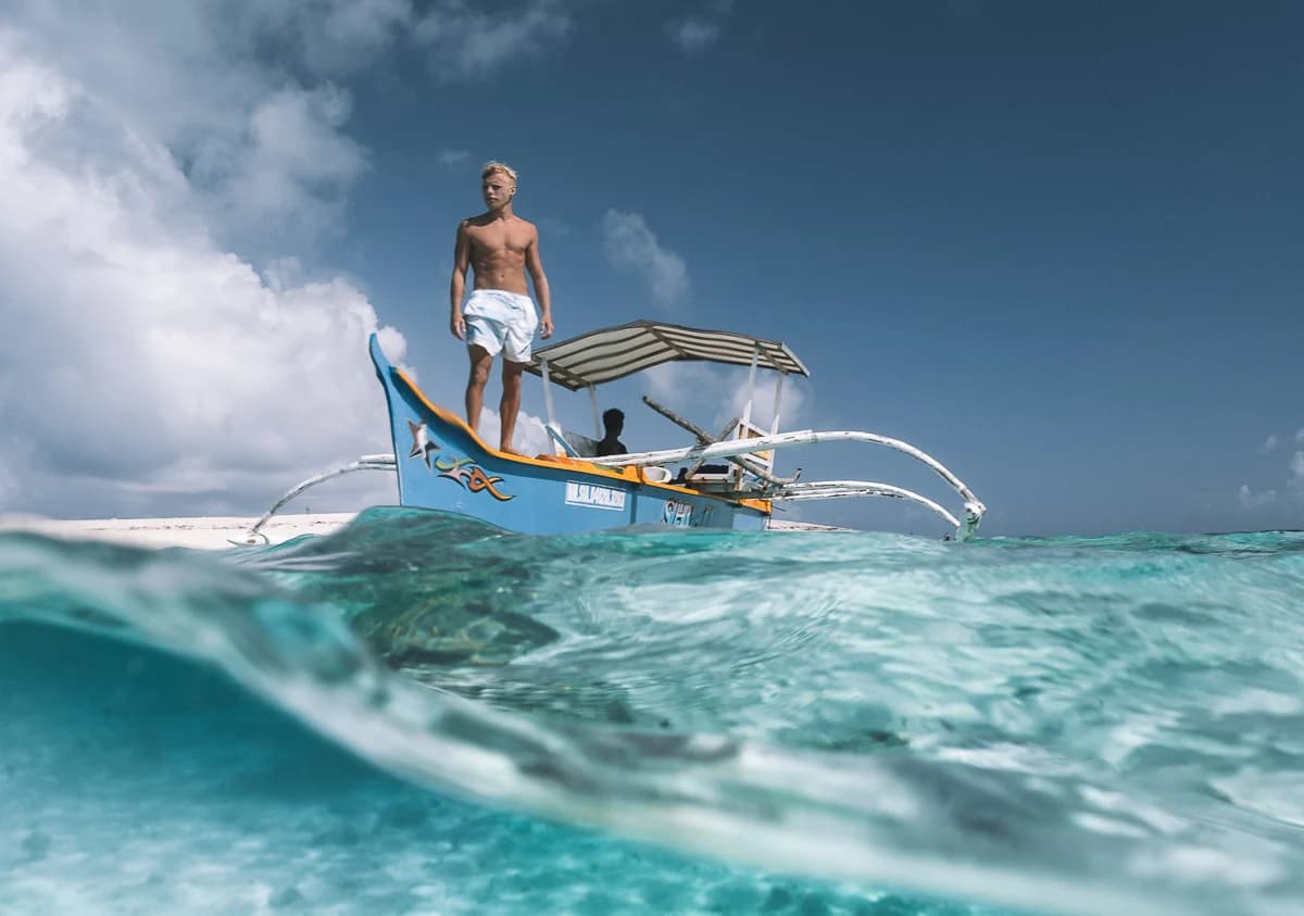 Half-in, half-out: the bangka idling over glass shallows between islands