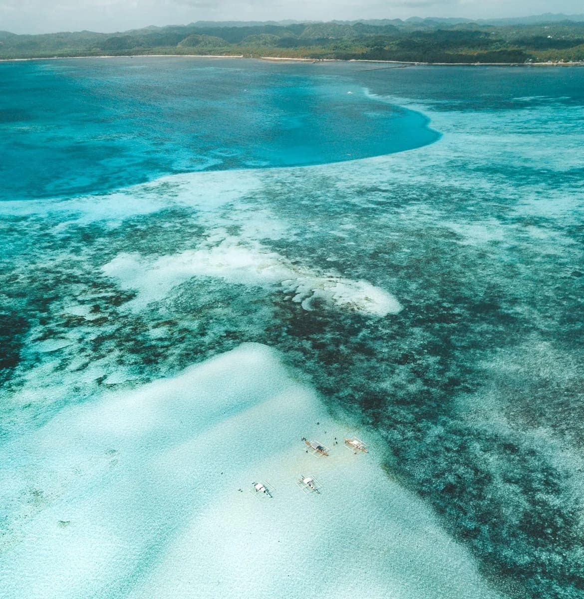 From altitude: bangkas parked on a bare sandbar with Siargao's coast beyond