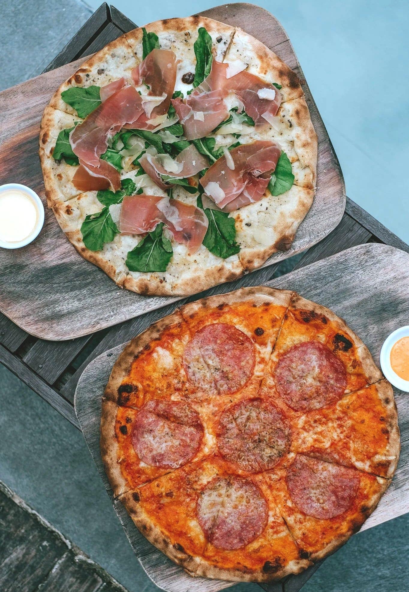 Parma ham and arugula pizza alongside a spicy salami pizza, straight off the wooden paddles