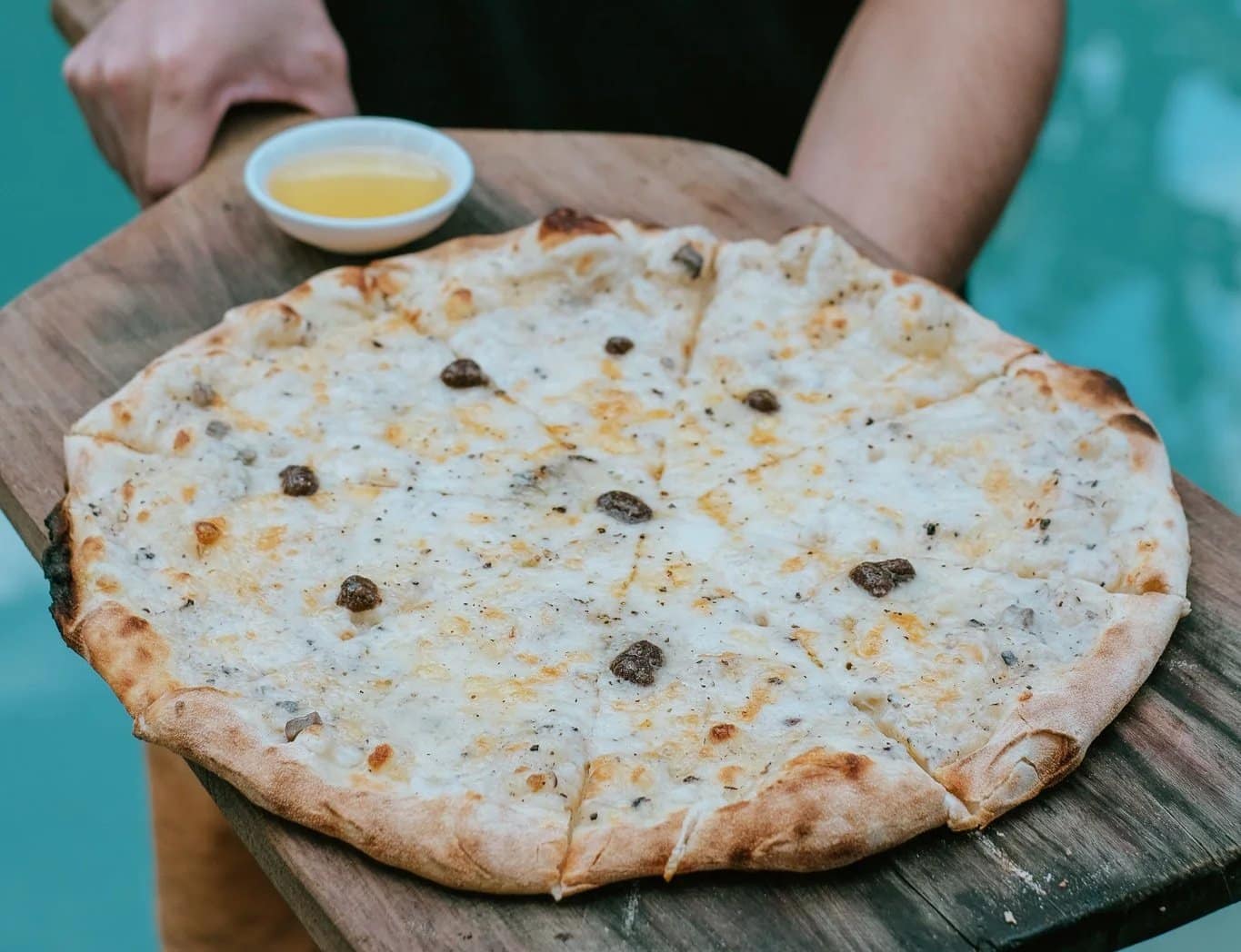 A blistered white pizza with truffle and melted cheeses, carried out on the board