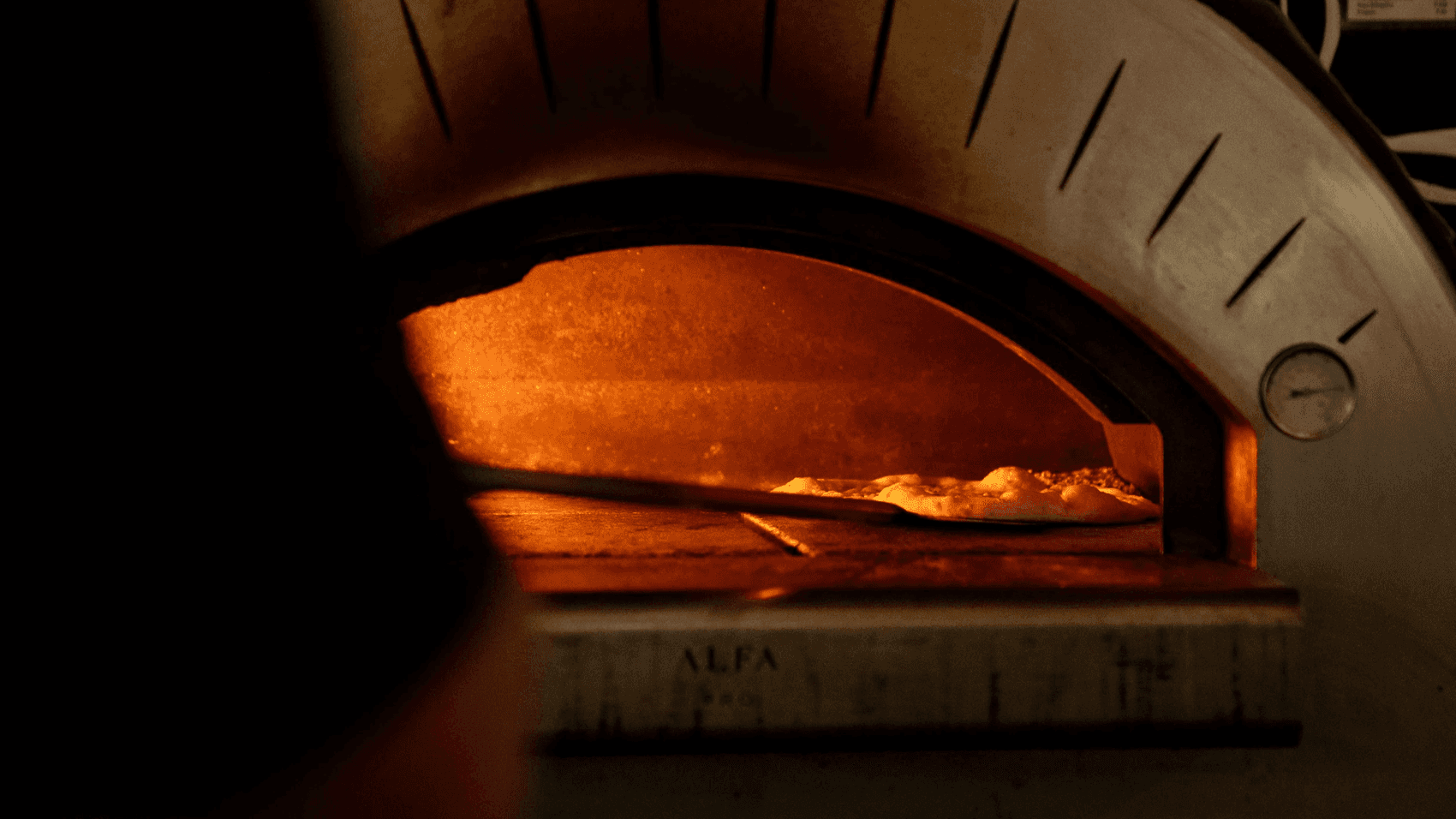 A pizza sliding into the glowing Alfa brick oven imported from Italy