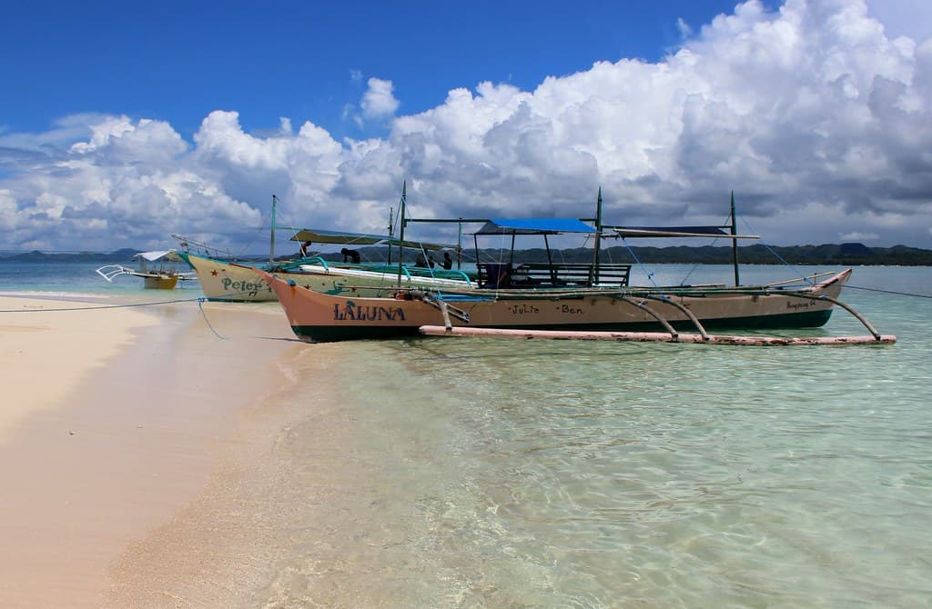 An outrigger bangka pulled up on a white sandbar under building cloud